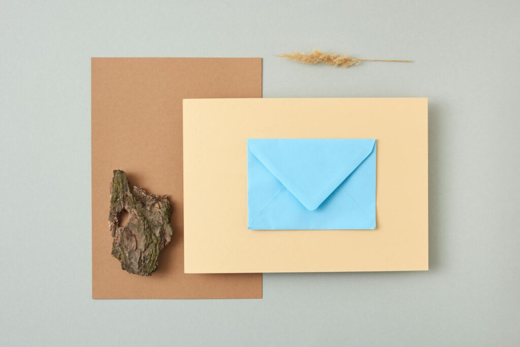 Flat lay image of a blue envelope on layered paper with natural elements. Perfect for creative design inspiration.