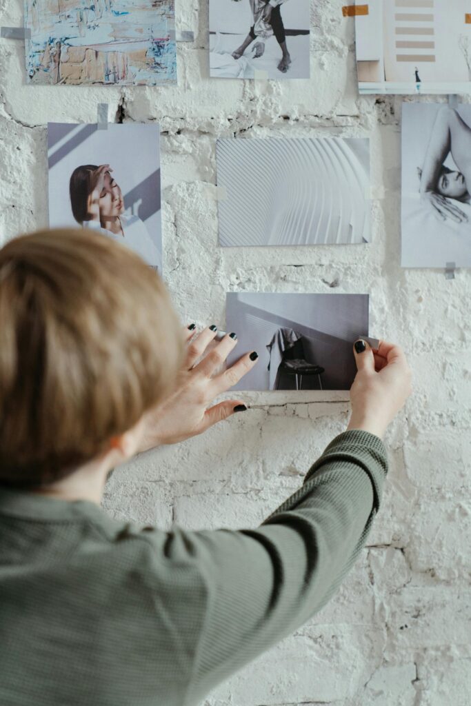 A woman is arranging a moodboard on a brick wall indoors.