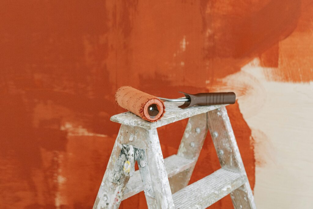 pexels-photo-5798984-5798984 Paint roller on a ladder with a partially painted red wall in the background.